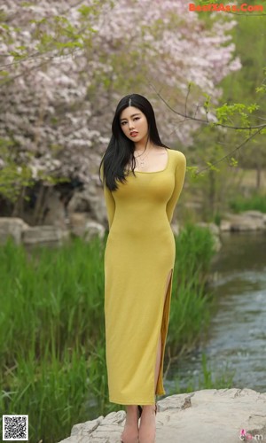 A woman in a yellow dress holding a pink flower.