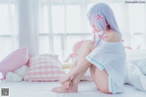 A woman in a pink dress sitting on a bed with a stuffed animal.