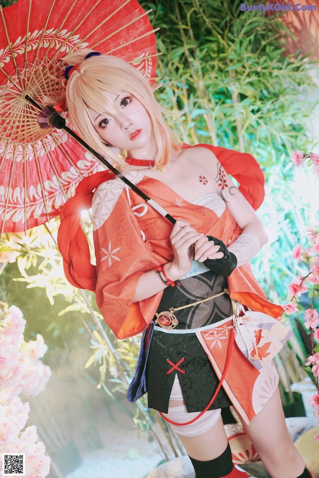 A woman in a kimono holding an umbrella in front of flowers.