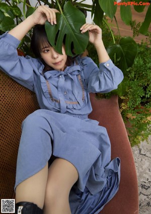A woman sitting on a chair in front of a plant.
