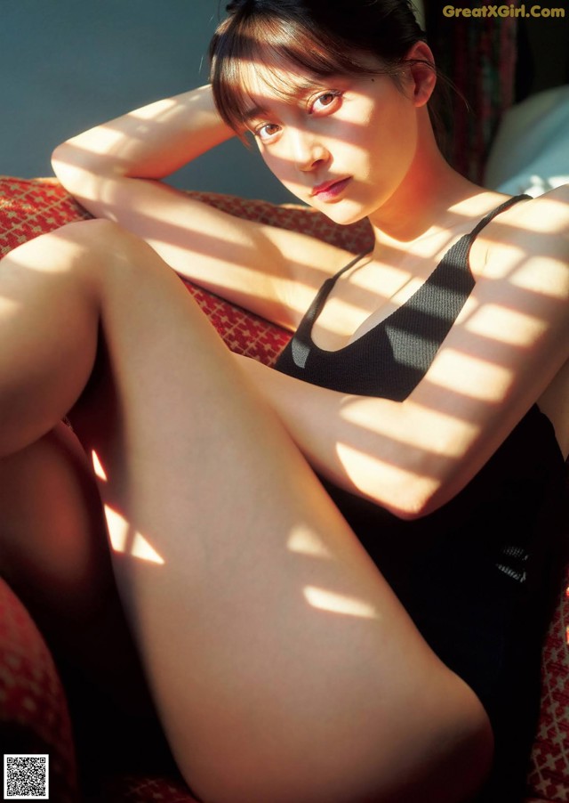 A woman in a black bathing suit sitting on a red couch.