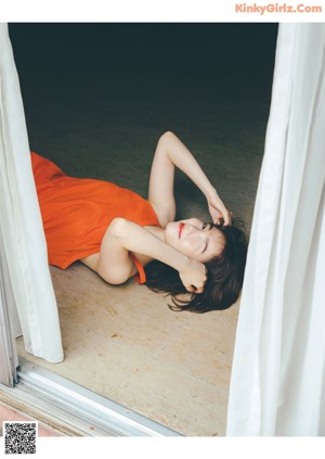 A woman in an orange dress leaning against a wall.