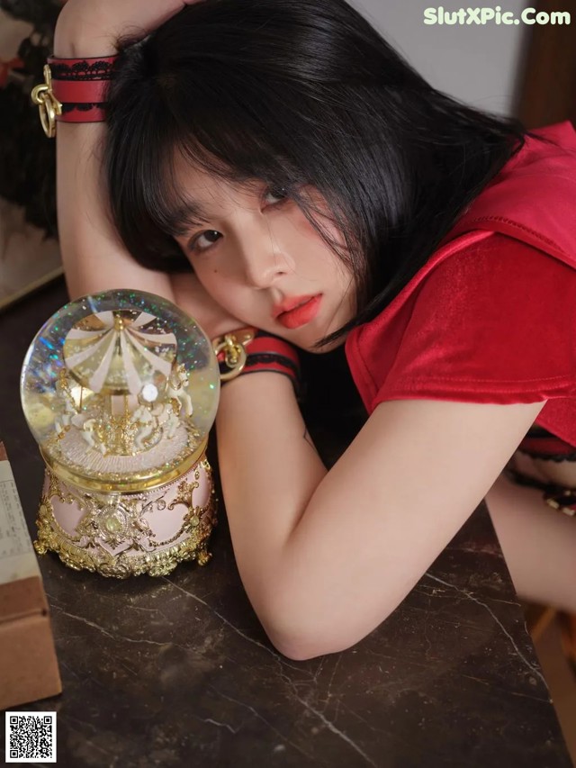 A woman in a red dress sitting at a table with a snow globe.