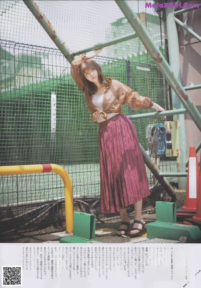 A woman in a pink pleated skirt leaning against a fence.