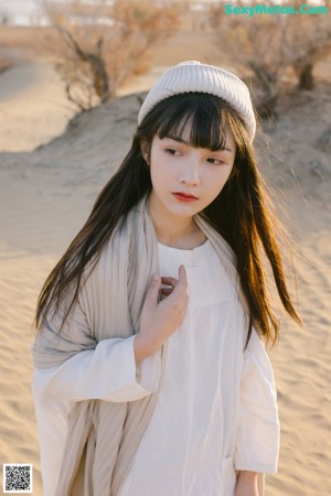 A woman standing in front of a tree wearing a white dress.