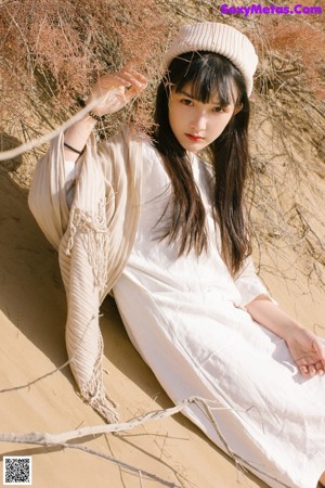 A woman in a white dress standing next to a tree.