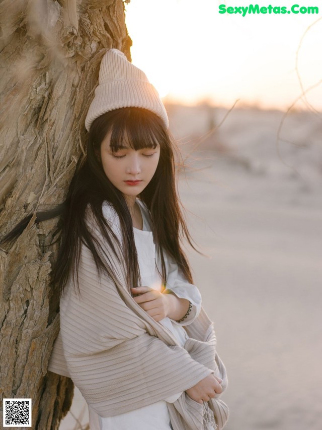 A woman leaning against a tree on the beach.