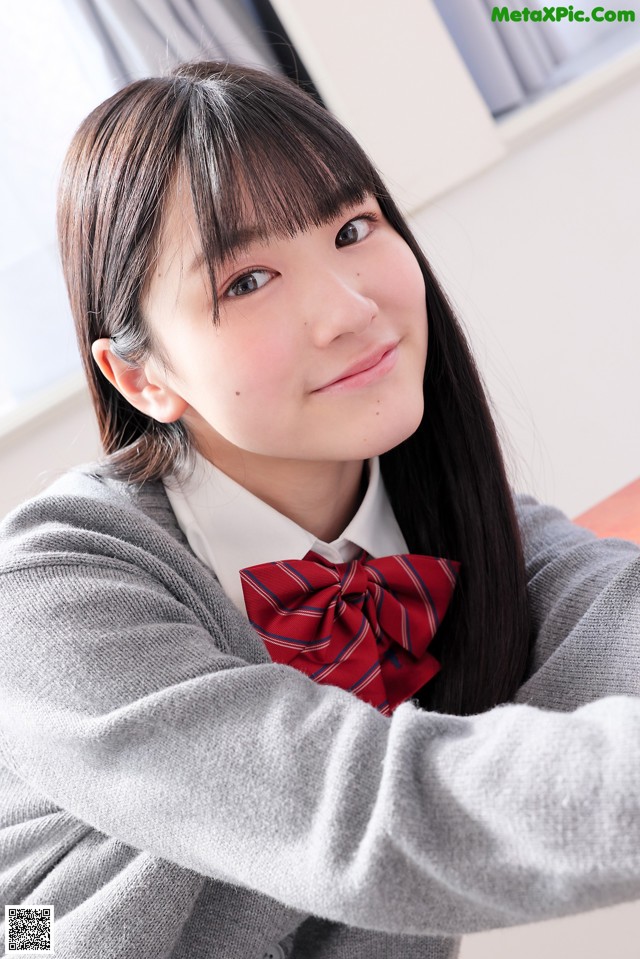 A young woman wearing a gray sweater and a red bow tie.