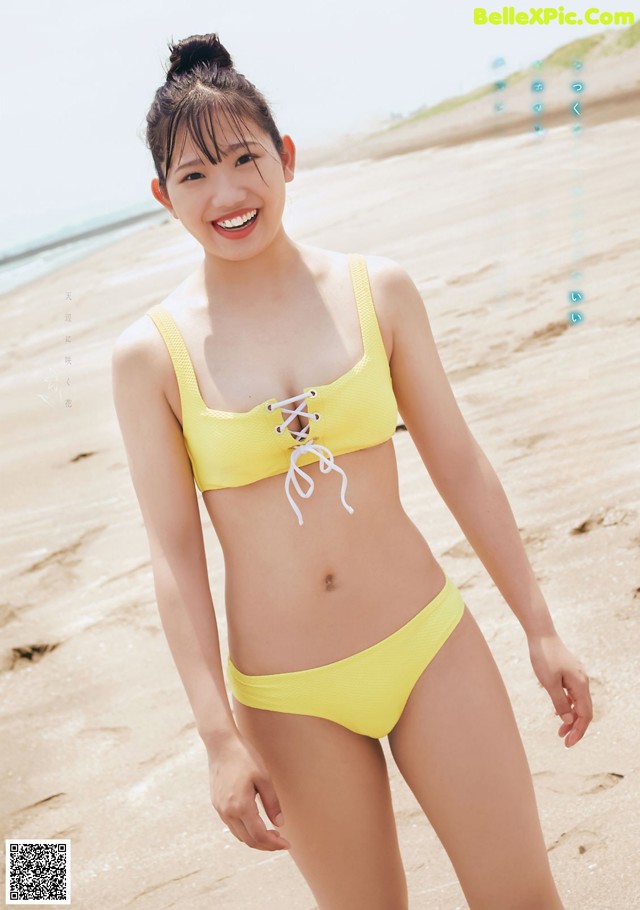 A woman in a yellow bikini standing on a beach.