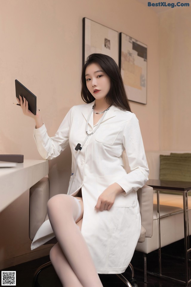 A woman in a white lab coat sitting at a desk.