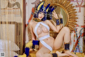 A woman dressed as an egyptian goddess sitting on a bed.