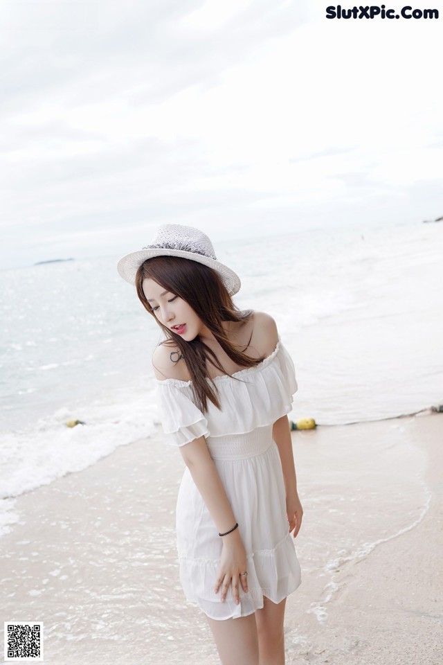 A woman in a white dress and hat standing on a beach.