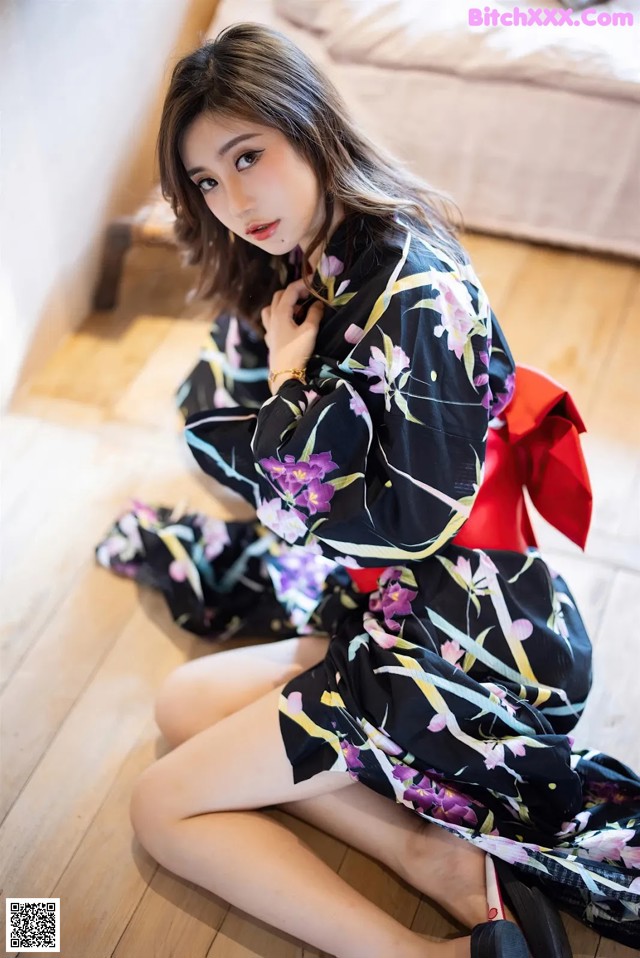 A woman sitting on the floor wearing a black and purple kimono.