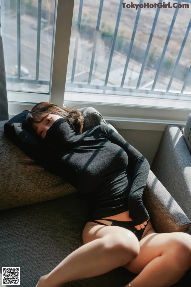 A woman laying on a couch in front of a window.