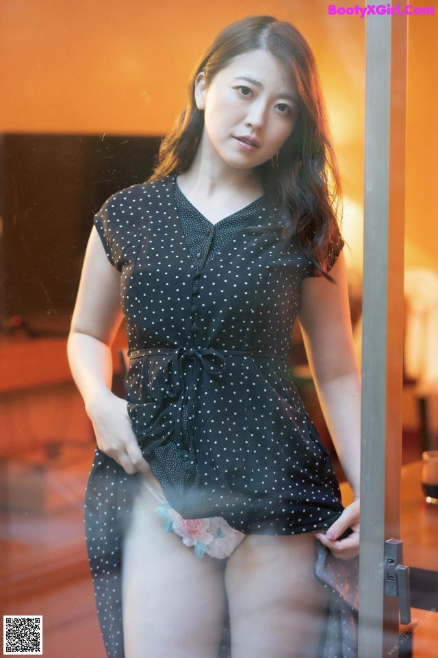 A woman in a black polka dot dress standing in front of a glass door.