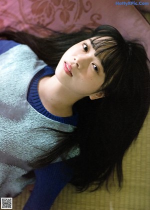 A young woman in a blue sweater is looking at the camera.