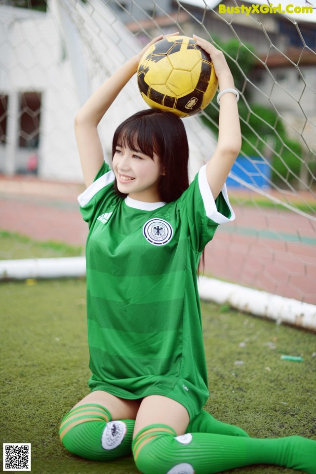 A woman in a green soccer uniform holding a soccer ball.