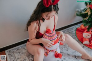 A woman in a red bathing suit sitting on the floor next to a Christmas tree.