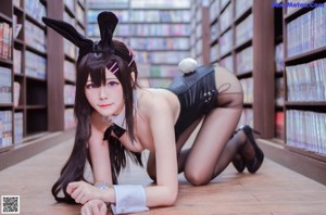 A woman in a bunny costume crouching down in front of a bookshelf.