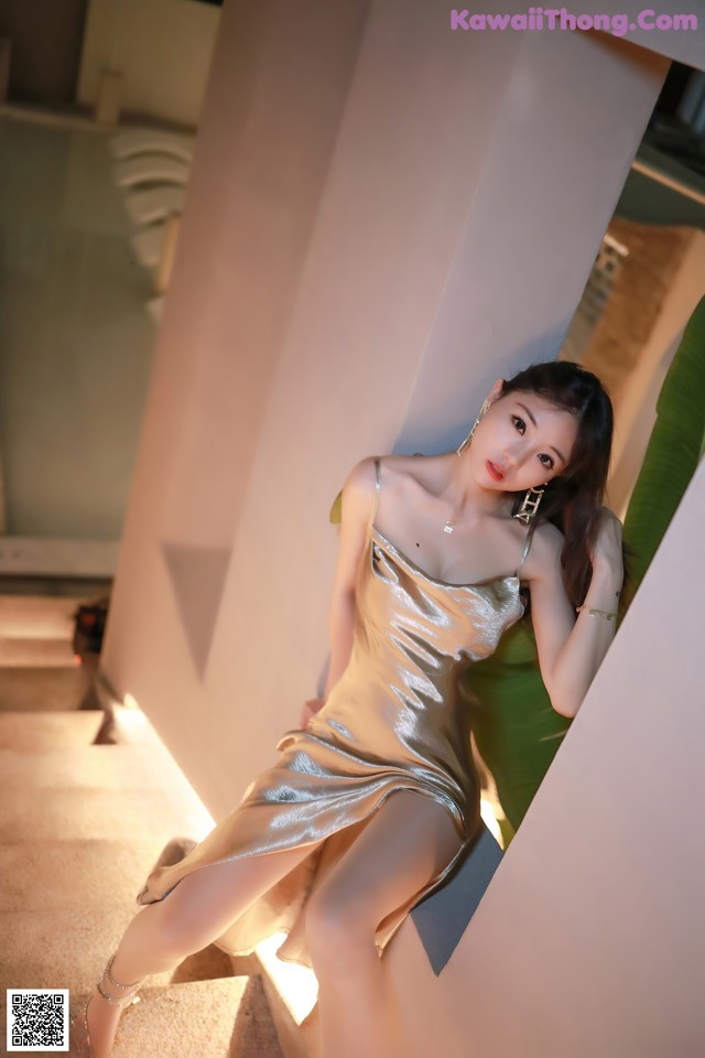 A woman in a gold dress leaning against a wall.