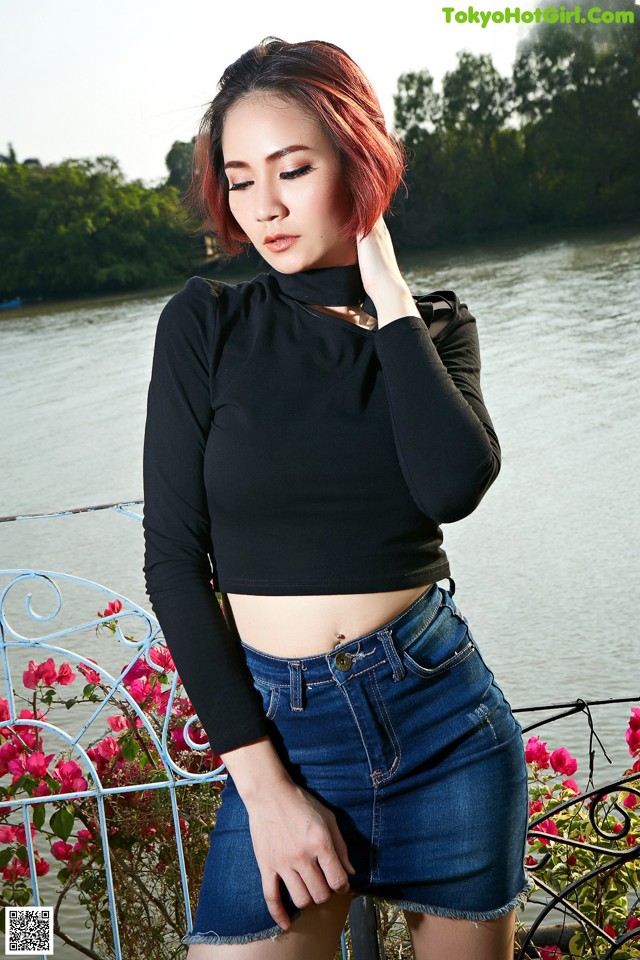 A woman in a black top and denim skirt posing by the water.